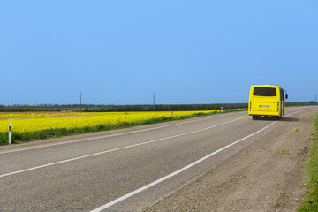 A yellow bus travels along the Auto Road overlooking the rapeseed fields.