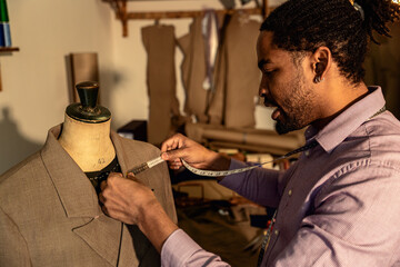Male fashion tailor working on the measurements for the suit design in his workshop.