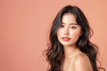 Fototapeta premium Softly lit portrait of an elegant woman with natural makeup posing on a light peach backdrop