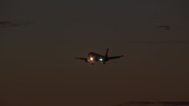 The plane with the landing gear released and the lights on is descending against the background of a twilight sky with gradient colors and clouds