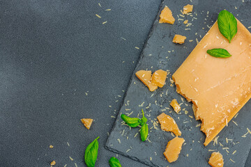 Piece of Parmesan cheese on modern stand. Garlic, fresh basil leaves, traditional Italian ingredient