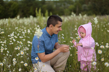 Smiling cheerful brunette Caucasian father and baby girl having fun on meadow among chamomile flowers man with infant daughter enjoying warm summer day