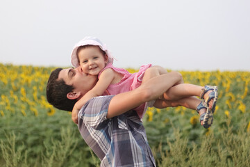Happy father's day. Father with little baby daughter in sunflowers field during golden hour dad and infant girl active in nature family walking in summer field.