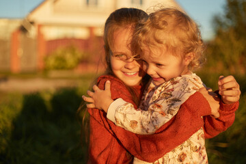 Sunny portrait of little cute charming sisters embracing each other while walking on street siblings hugging with love and tenderness expressing happiness while playing together outdoor