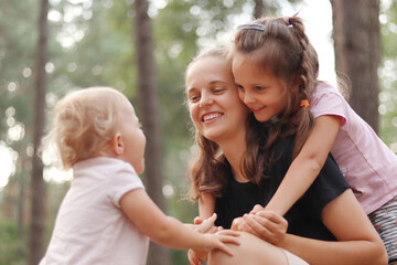 Kids congratulating mommy with mother's day. Happy Caucasian family playing in sunny park woman hugging with her daughters smiling happy enjoying pleasant family moments during summer walk outdoor