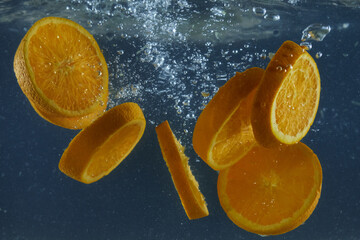 Tropical oranges dropped into water with air bubbles isolated over dark blue background