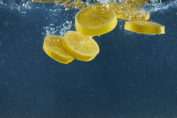 Yellow lemon slices falling in water for making cocktail isolated on blue background, empty space for advertisement content