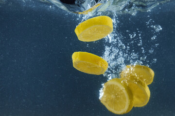 Fresh lemon slicers falling in water with splashing isolated over dark blue background, copy space