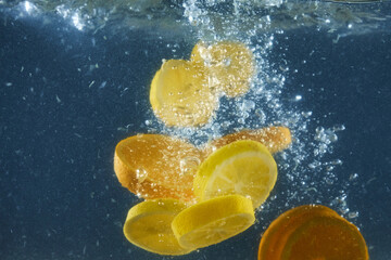 Tropical fruits oranges and lemons dropped into water with splashing isolated over dark blue...