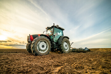 Wide-angle view of a tractor plowing farmland against a dramatic sunset sky