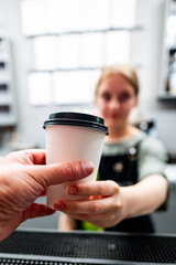 Blurred figure of a person holding a takeaway coffee cup, with a focus on the cup against a modern cafe background