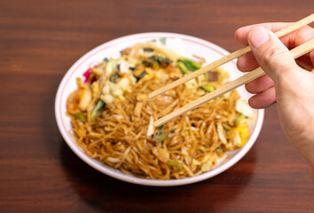 Fried noodle with chicken and vegetables in a white bowl on a wooden table. After edits.