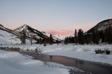Sunrise reflected in a stream amidst a snow-covered landscape near Crested Butte, Colorado.