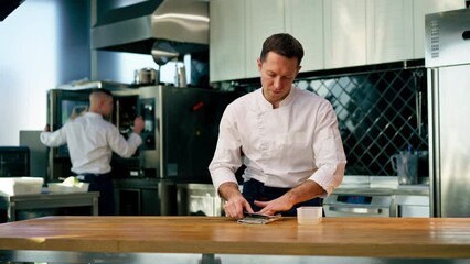 a chef in a white jacket in the kitchen at the table sharpens knife on a green stove