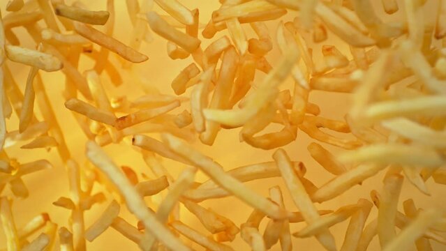 Super Slow Motion Shot of French Fries Flying Towards Camera on Golden Background at 1000fps.