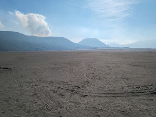 A sea of sand against the backdrop of a volcano whose crater is still actively emitting volcanic...