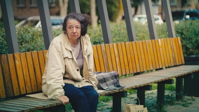 Untidy elderly woman sitting alone on bench, homeless person needs shelter