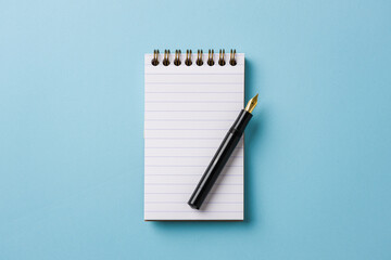 Top view of notebook and fountain pen on blue background
