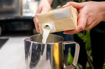 A person pouring milk from a carton into a stainless steel jug, illustrating a common kitchen scene