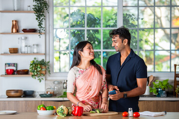 Indian asian smart young couple using smartphone in modern kitchen