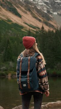 Woman traveler hipster with backpack walking near lake and looking forward at amazing mountains