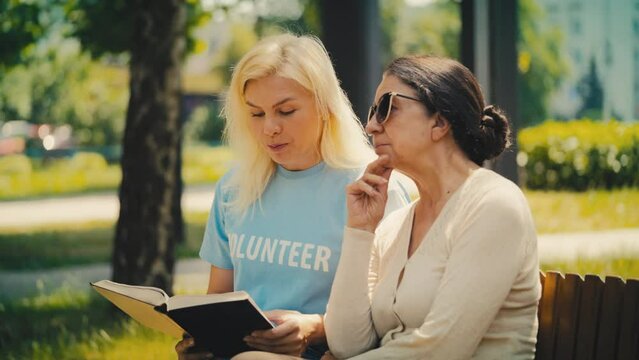 Kind female volunteer reading to senior woman in park, retirement home care