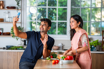 Indian asian smart young couple using smartphone in modern kitchen