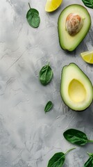 Fresh avocado cut in half with basil leaves and lemon wedges on a textured background