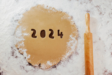 2024 numbers carved on gingerbread dough on white four and rolling pin