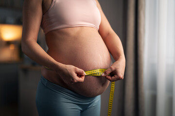 A close-up shot of an unrecognizable pregnant woman measuring her belly