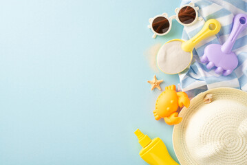 Beach play essentials for kids. Top view of sand toys: shovel, rake, crab mold, SPF cream, straw hat, sunglasses, beach blanket, shell, starfish on pastel blue with copy space