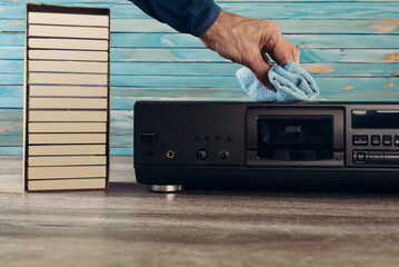 Closeup photo of man cleaning old retro tape recorder with microfiber cloth. Vintage audio: Wooden cassette tape recorder with cassettes, perfect for nostalgic music lovers