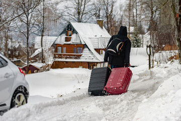Male tourist with luggage arriving at snowy cabin in mountains, Luggage in hand, a man ventures into a snowy wonderland for vacation