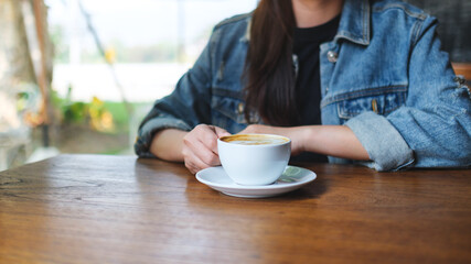 Closeup image of a woman holding and drinking hot coffee in cafe