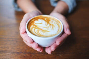 Closeup image of a woman holding a cup of hot coffee with latte art