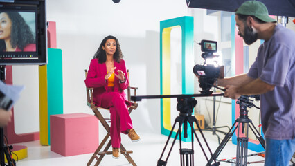 Vibrant Film Set Captures Young South Asian Female Host In A Pink Suit Engaging In A Lively...