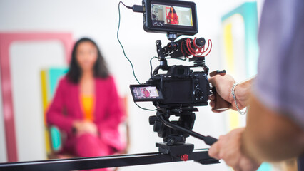 Vibrant Scene Captures Young Asian Female Host In Pink Blazer On Film Set, Engaging In Lively...