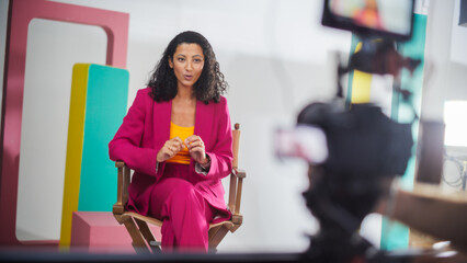 Young Black Female Host In Vibrant Pink Suit Engaged In Lively Discussion On Colorful Set, Captured...