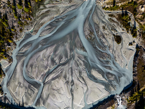 Overhead image captures the intricate patterns of a braided river system surrounded by rugged terrain, highlighting nature's artwork