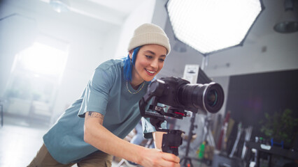 Focused Young Caucasian Female Videographer Adjusts Professional Camera In Well-lit Studio, Capturing Essence Of Modern Filmmaking And Creativity In Advertising Production.