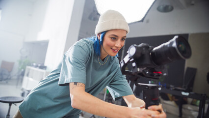 Young Female Cinematographer With Blue Hair Adjusts Professional Camera In A Bright Studio Setting,...