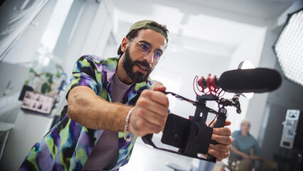 Young Latin Male Videographer With Beard, Wearing Colorful Shirt And Headband, Operates Camera With...