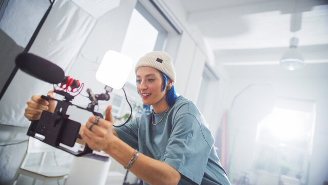 Young Caucasian Female Filmmaker With Blue Hair, Wearing A Beanie, Operates A Professional Camera In A Well-lit Studio, Capturing Engaging Content For A Creative Advertising Project.