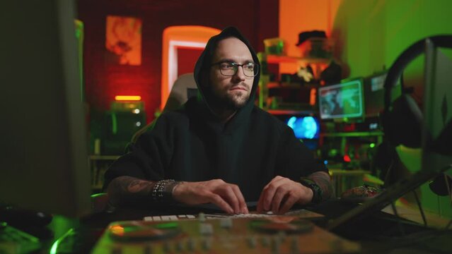 Hacker writing code cracking computer. Man programmer in hoodie cracks system, using computer in dark room. Hacker attack, technology, virus infected software, dark web and encryption concept.