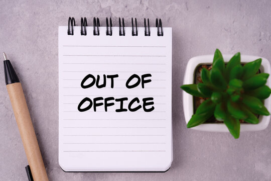 Workplace environment and situation concept. OUT OF OFFICE written on a notepad. Blurred styled background.