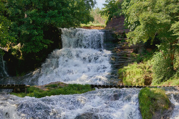 Cascade waterfall in rocks overgrown with trees and greenery
