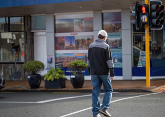 Man walking across the road with pedestrian traffic signal on. Tourism advertisements on display at the windows of a Travel Shop. Auckland. - 792616756