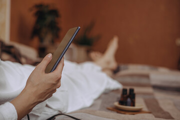 Crop woman with smartphone in hand lying on bed and relaxing on weekend at home 