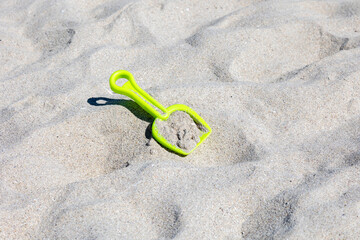 A vibrant green shovel stands out on a sandy beach, bathed in sunlight, suggesting summer fun and...