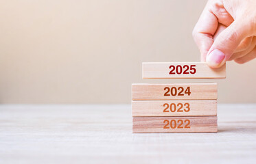 2025 block over 2024 and 2023 wooden building on table background. Business planning, Risk...